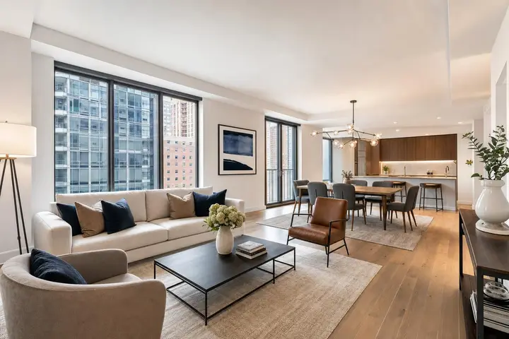 Modern NYC apartment living room with stylish decor, cozy seating area, and large windows overlooking city buildings.
