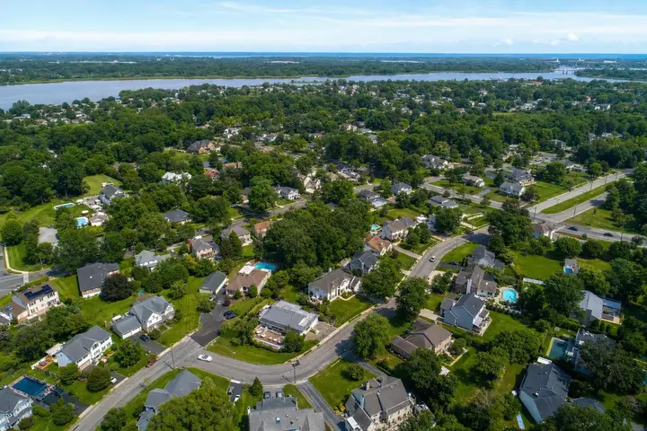 Aerial view of a suburban neighborhood with tree-lined streets, houses, and a river in the background, showcasing drone photography NJ.