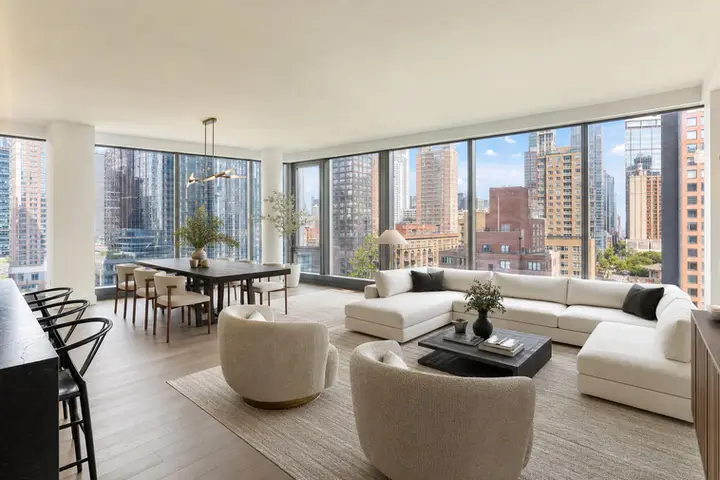 Spacious modern living room and dining area with large windows overlooking NYC skyline, showcasing luxury interior design.