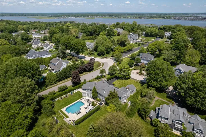 Aerial drone view of a large suburban home with manicured lawn, driveway, and surrounding trees, perfect for real estate showcasing