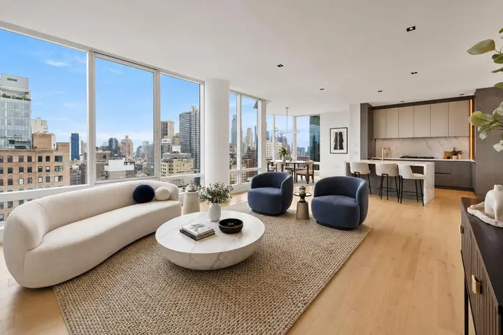 Modern living room with city views, featuring a curved sofa, round marble table, and sleek open kitchen in NYC.