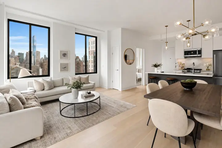 Spacious modern apartment interior with large windows showcasing NYC skyline, elegant decor, and open-plan kitchen and living area.