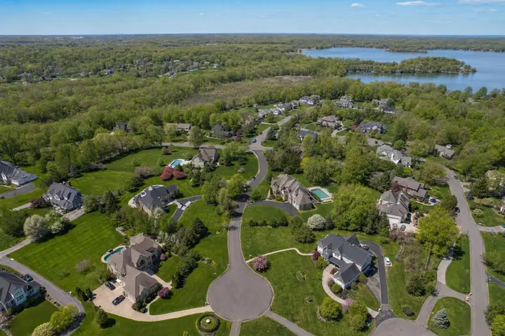 Aerial view of a lush suburban neighborhood in New Jersey with homes, greenery, and a distant lake visible.