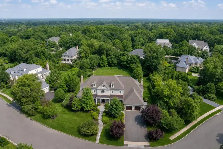 Aerial view of a suburban neighborhood with large houses surrounded by lush greenery and tree-lined streets.