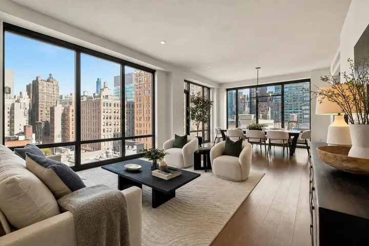 Modern NYC living room with large windows showcasing city views, stylish furniture, and elegant decor.