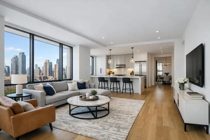 Modern open-plan living room with city skyline views, featuring a cozy seating area, kitchen island with bar stools, and decor.