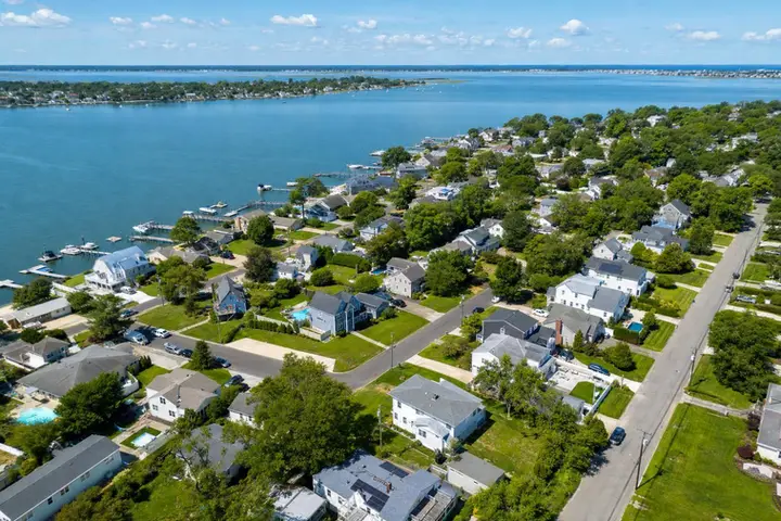Aerial view of a suburban neighborhood by a body of water, showcasing homes, greenery, and a scenic shoreline in NJ.