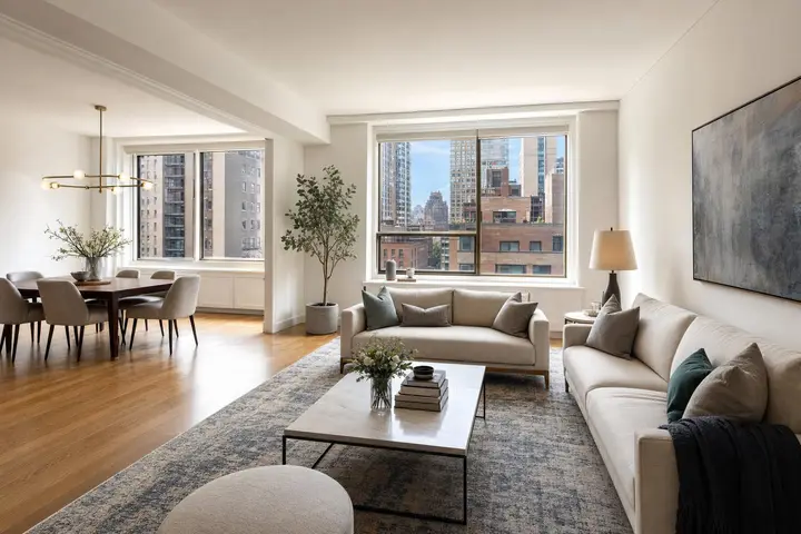 Bright modern living room and dining area featuring large windows with city views, neutral sofas, and elegant decor.