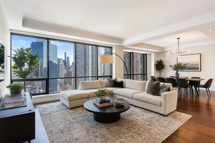 Spacious NYC living room with large windows showcasing city skyline, elegant furniture, and a stylish dining area.