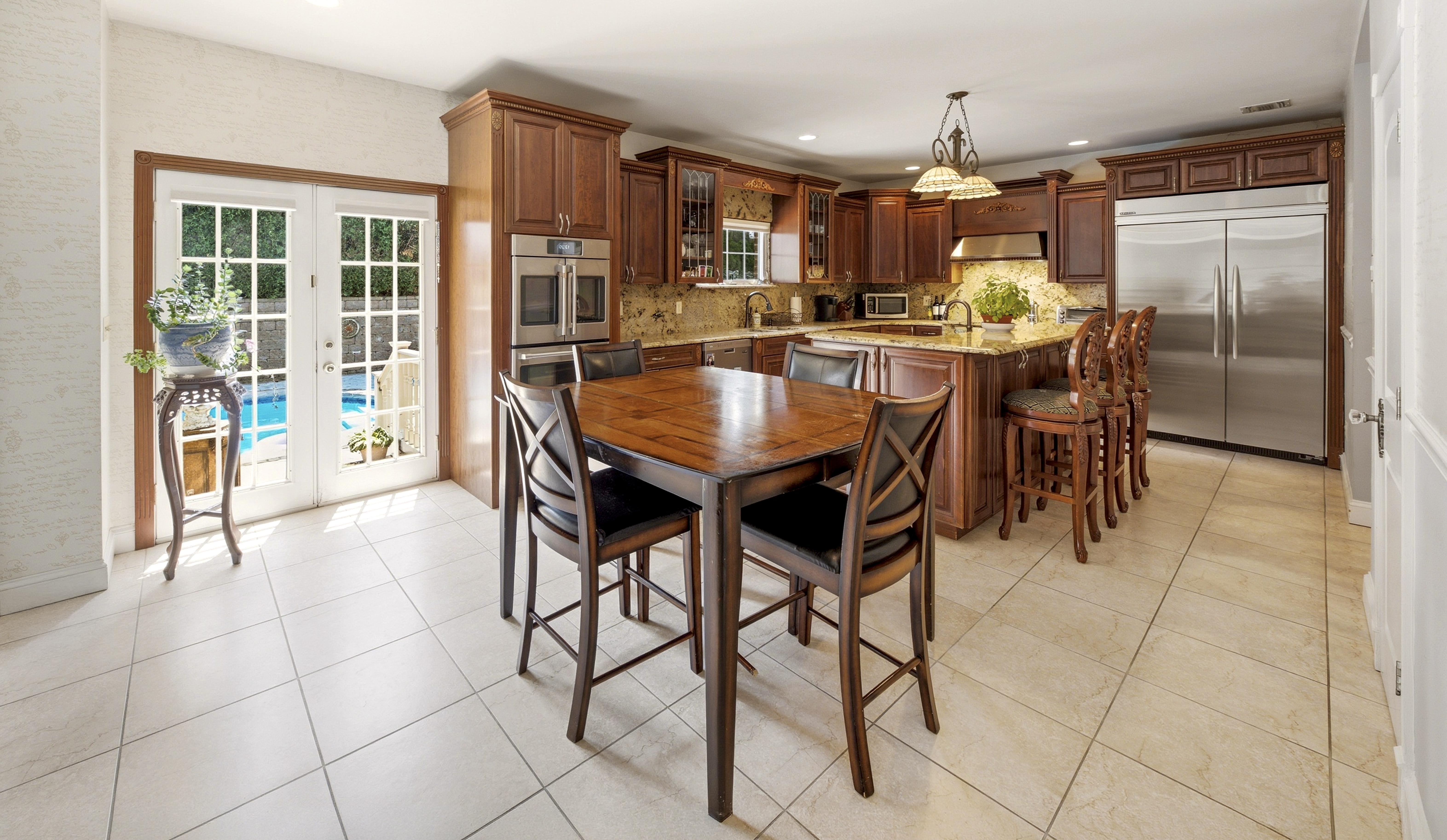 Staten Island single-family home eat-in kitchen with wood cabinetry, granite counters, tile floors and French doors opening to a pool patio — HDR real estate photo